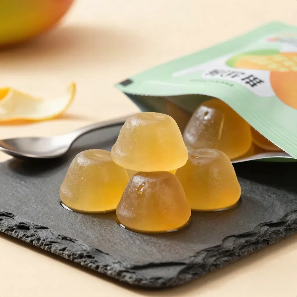 Mango gummies on a slate tray with citrus peel and a metal spoon, close-up.